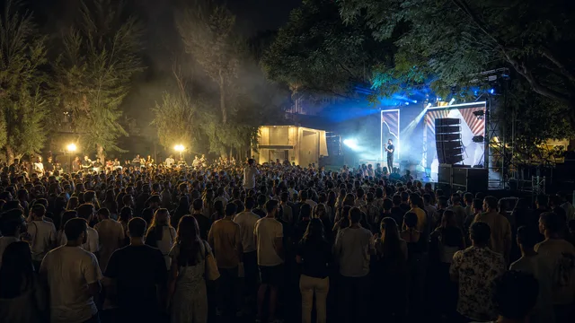 An illustrative night concert at Radzyner Square, with students beneath the trees and a blue-lit stage